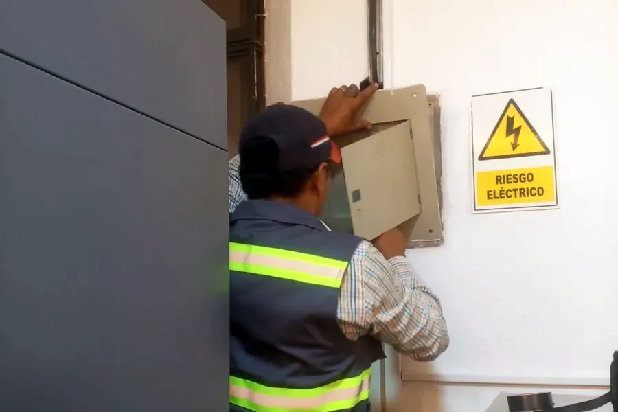 Técnico abriendo un tablero eléctrico junto a una señal de riesgo eléctrico